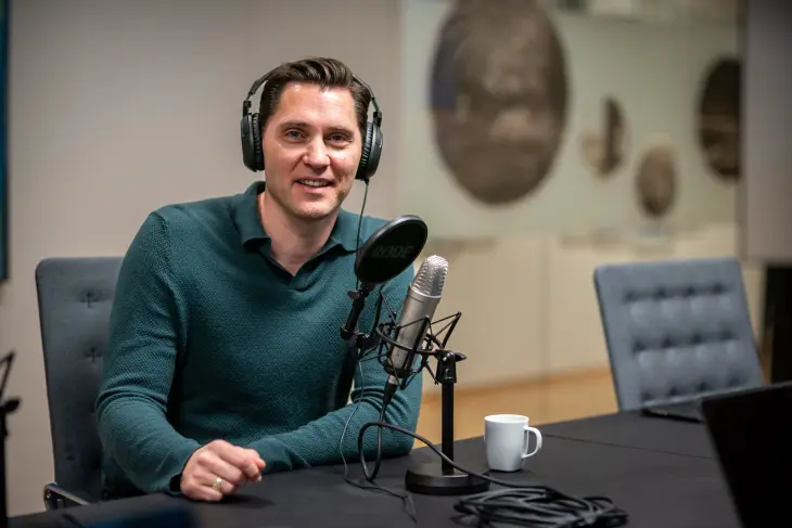 Mann som sitter smilende i et podcaststudio